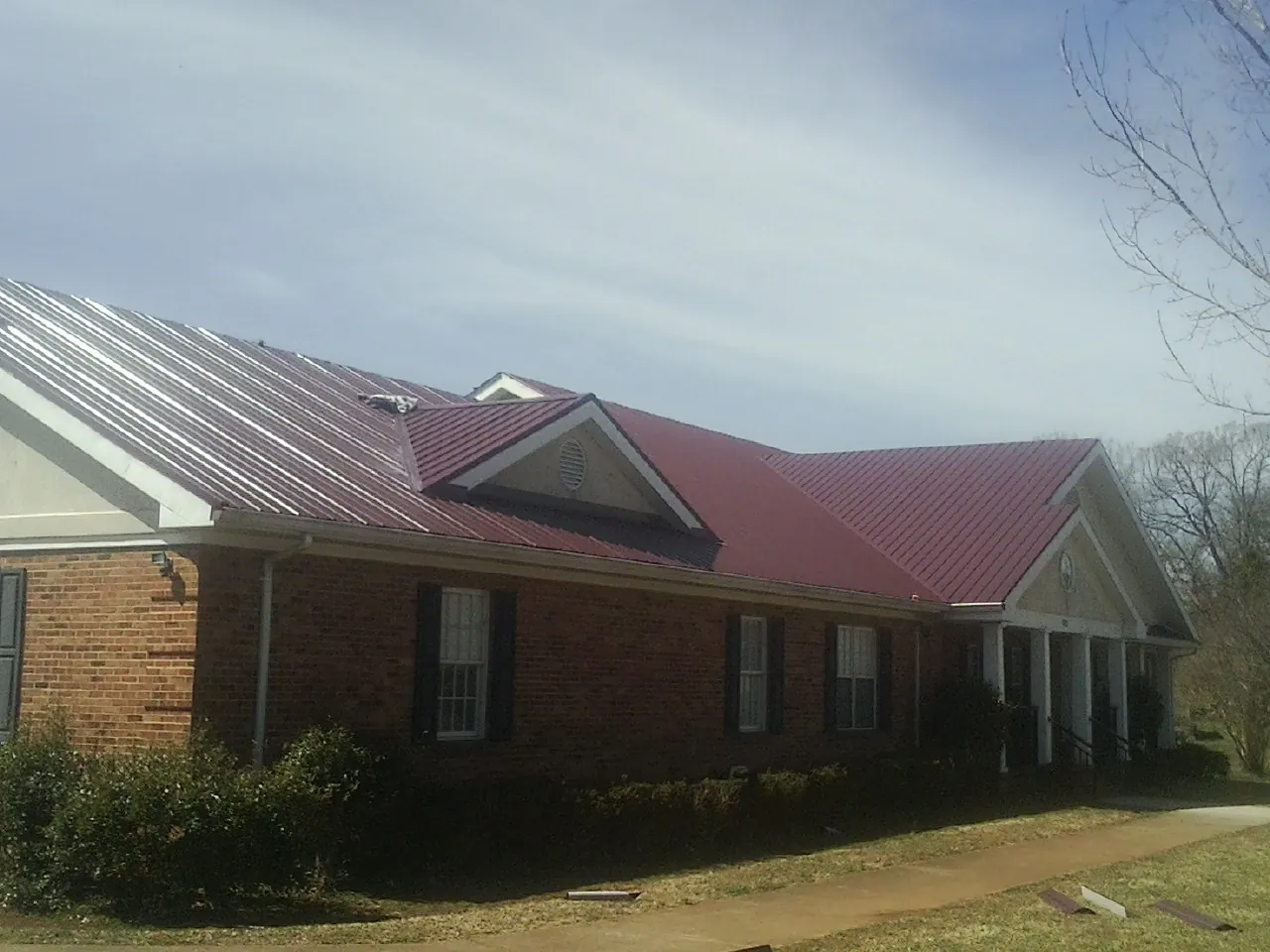 Red metal roof with gabled entries on a long brick building, from a Hail Damage Roof Repair job in Diablo