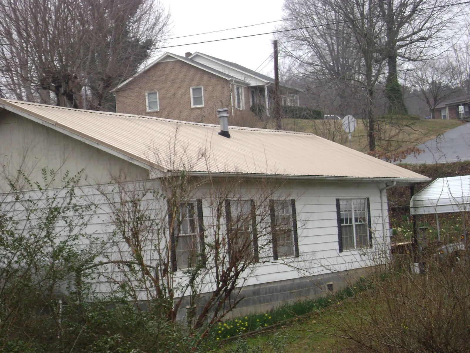 Tan metal roof on a white sided house set into a hillside — Commercial Roofing by Roofing Brothers in Diablo